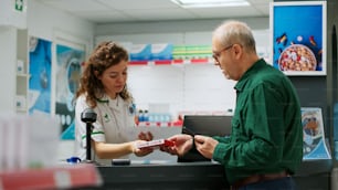 Medical worker helping senior man with prescription medicine, giving treatment pills and medicaments at pharmacy counter. Elderly client asking for healthcare drugs and vitamins to cure disease.