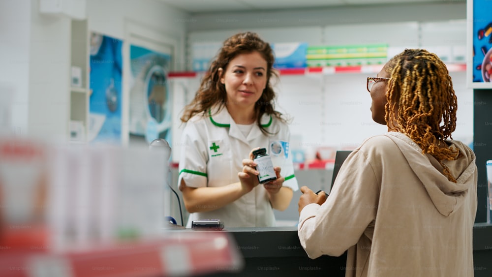 African american person asking pharmacist about prescription treatment in bottle of pills to buy from pharmacy shop. Medical worker serving woman with pharmaceutical products and medication.