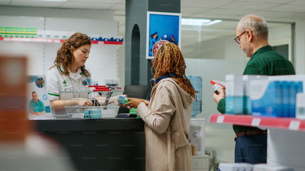 Pharmacist helping african american woman to buy medicaments and healthcare treatment at drugstore counter. Employee scanning boxes of pills and vitamins to sell pharmaceutics.