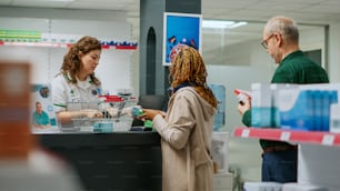 Farmacêutico ajudando mulher afro-americana a comprar medicamentos e tratamento de saúde no balcão da farmácia. Funcionário escaneando caixas de pílulas e vitaminas para vender produtos farmacêuticos.