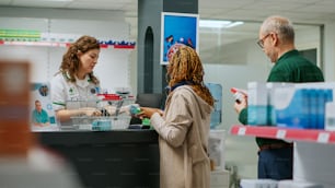 Pharmacist helping african american woman to buy medicaments and healthcare treatment at drugstore counter. Employee scanning boxes of pills and vitamins to sell pharmaceutics.