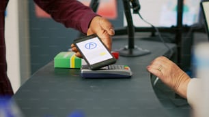 Male client buying vitamins with mobile phone nfc payment, using smartphone at pos terminal in drugstore. Person paying for medicaments and drugs at pharmacy counter. Close up. Handheld shot.