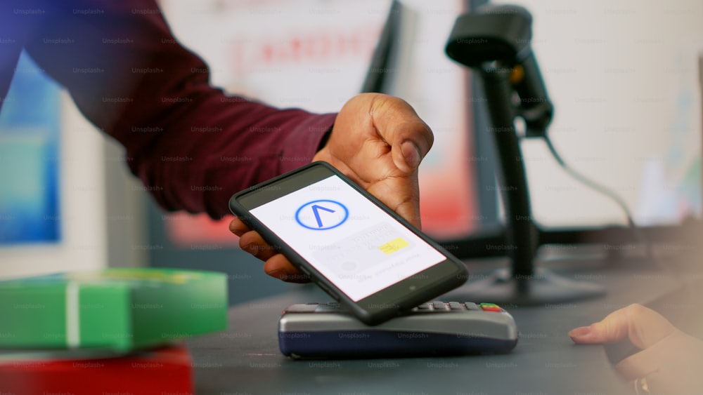 Junger Mann, der Medikamente mit Handy-NFC-Zahlung kauft, mit dem Smartphone am POS-Terminal in der Drogerie. Person, die Medikamente und Medikamente an der Apotheke bezahlt. Aufschließen. Stativ geschossen.