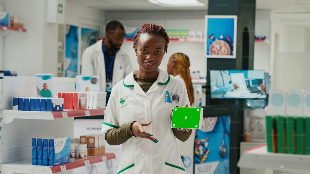 Specialista della salute che indica la scatola della medicina con schermo verde, come modello di chroma key isolato nel negozio di farmacia. Giovane impiegato che tiene sfondo copyspace vuoto in farmacia.