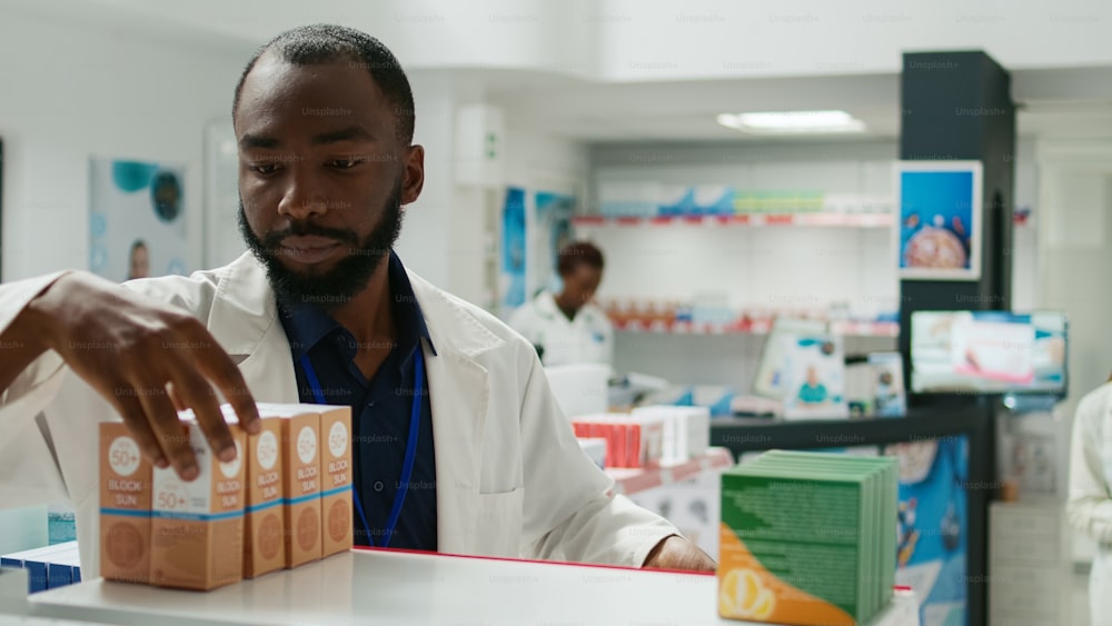 Pharmacy employee arranging stock of medicaments on drugstore shelves, putting boxes of pills and vitamins to help customers. Young man working with pharmaceutical products, retail store.