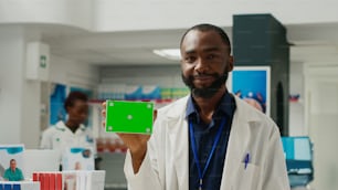 Pharmacy consultant holding greenscreen on box of drugs, showing blank copyspace template in drugstore. Doctor recommending medicaments with isolated mockup chromakey background pack.
