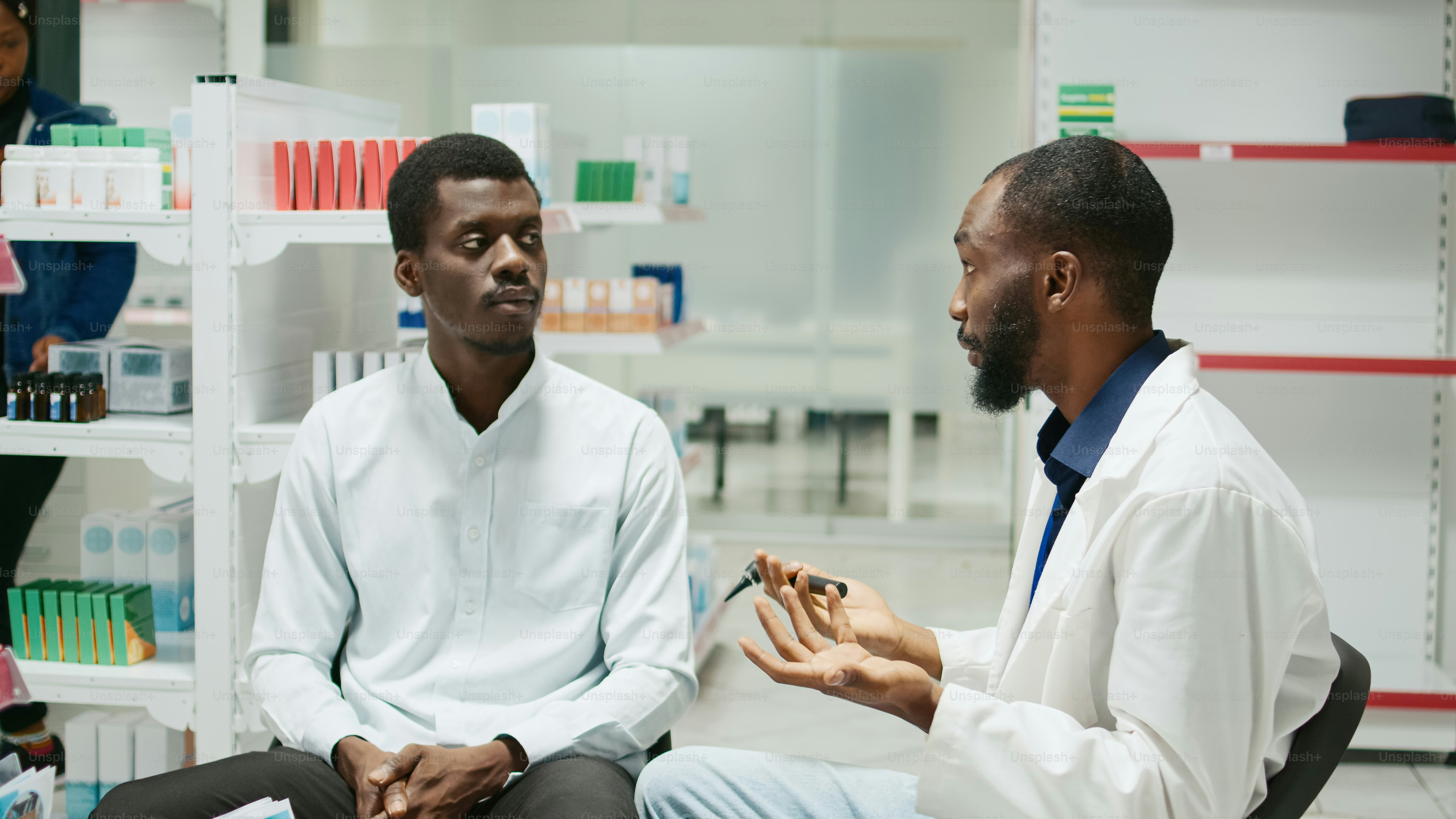 男性医師がクリニックで耳鏡で顧客に相談し、ドラッグストアに座って耳の検査を行います。耳鼻咽喉科の相談のために感染をチェックする若い耳科医とクライアント。