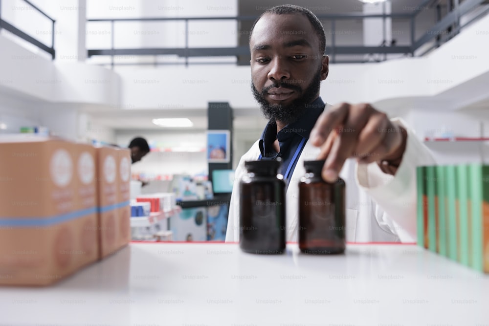 Farmacêutico afro-americano colocando frascos de pílulas na prateleira da farmácia, foco seletivo. Vendedor de farmácia tomando pacotes de medicamentos de perto, vendendo suplementos, vista frontal