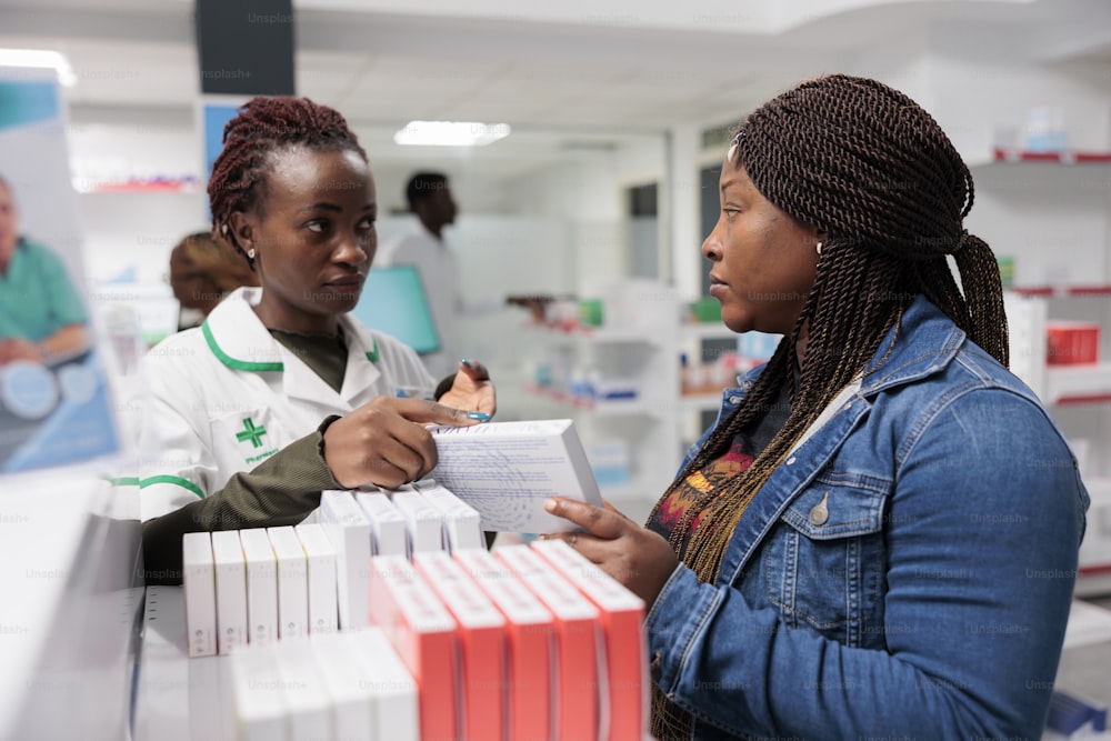 Assistente de farmácia afro-americano consultando comprador em farmácia, mulher escolhendo medicamentos, comprando vitaminas. Medicamentos de varejo, farmacêutico ajudando o cliente, explicando a instrução de pílulas