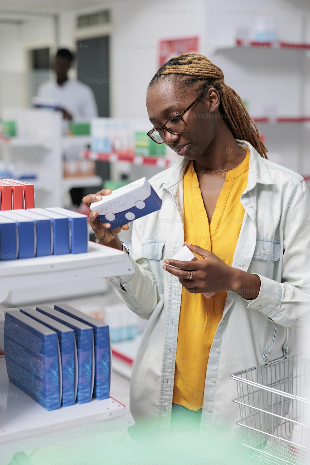 Mulher afro-americana verificando multi vitaminas na prateleira da farmácia, olhando para pacotes de comprimidos. Cliente escolhendo suplementos nutricionais, cliente em pé no corredor da loja da farmácia