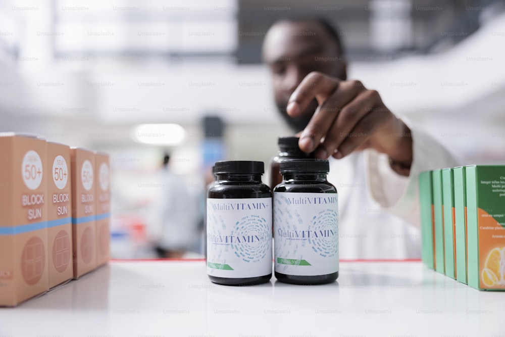 Farmacista afroamericano che prende vitamine dal primo piano dello scaffale della farmacia, attenzione selettiva alle bottiglie. Farmacia medica mettendo le pillole vista ravvicinata, vendita di integratori, servizio farmaceutico