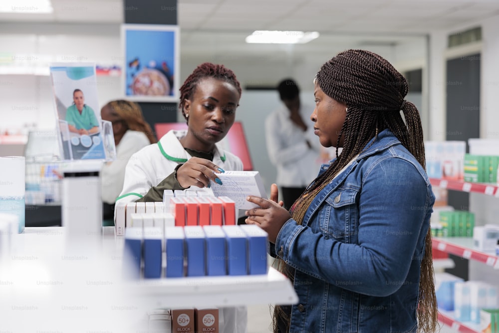 African american pharmacist showing customer medications on drugstore shelf, woman buying vitamins. Medicaments retail, pharmacy consultant helping client choosing medications