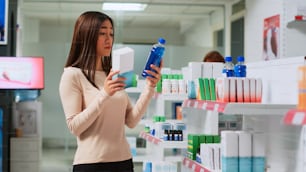 Young woman reading pharmaceutics leaflet in drugstore, checking medicaments to buy healthcare products. Customer looking at pills boxes to buy prescription treatment or medicaments.