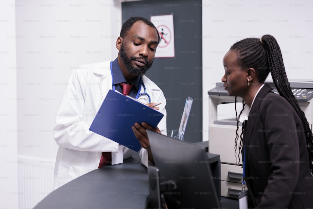 病院の受付で医療レポートに取り組み、患者の予約を書類で分析するアフリカ系アメリカ人のスタッフ。病気の人を助けるために健康診断フォームを使用する医師と受付係。