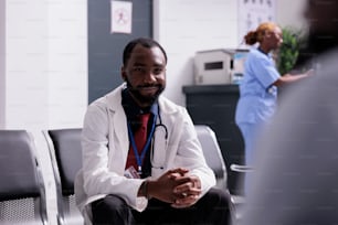 Portrait of african american medic in hallway, sitting in waiting room seats before having medical consultation appointment with patients. General practitioner working on healthcare in center.