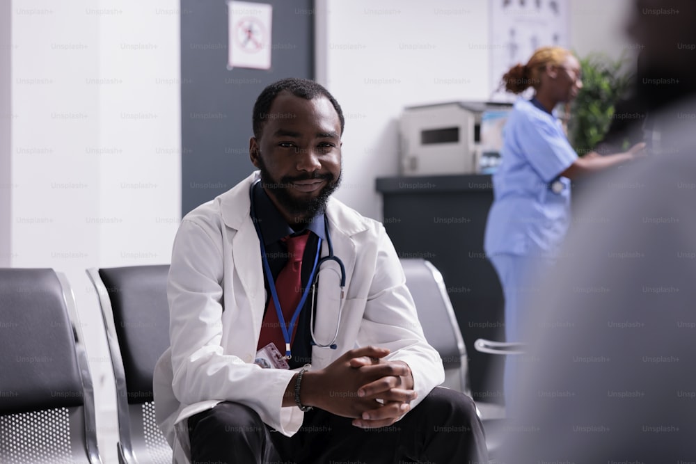 Portrait d’un médecin afro-américain dans le couloir, assis dans les sièges de la salle d’attente avant d’avoir rendez-vous en consultation médicale avec les patients. Médecin généraliste travaillant sur les soins de santé en centre.