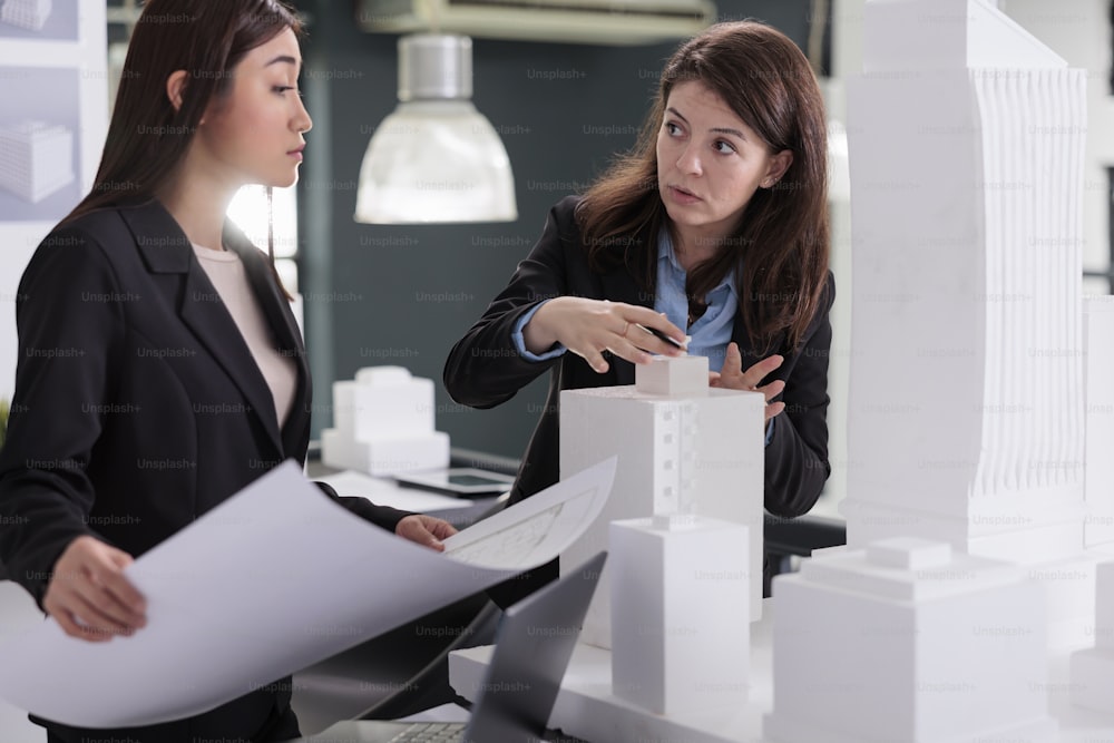 Arquitectos discutiendo planos, sosteniendo borradores de proyectos de construcción de edificios, coworking en oficinas de arquitectura. Diseñadores en equipo, trabajadores inmobiliarios hablando de bocetos industriales