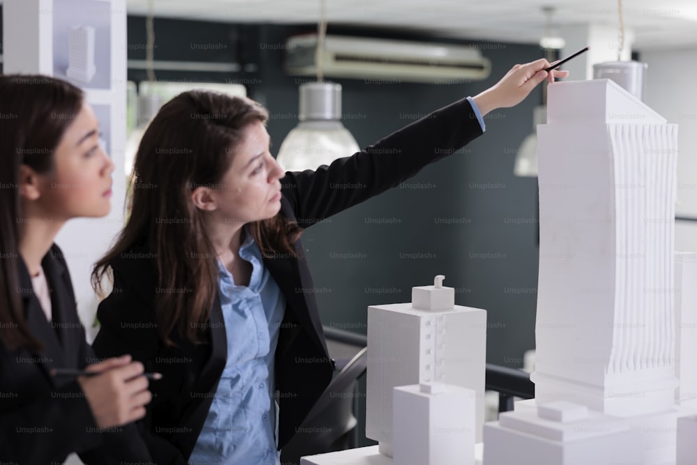 Real estate agency employees coworking, discussing building 3d model, brainstorming ideas in meeting. Architects thinking on city house construction project, looking at mock up building.