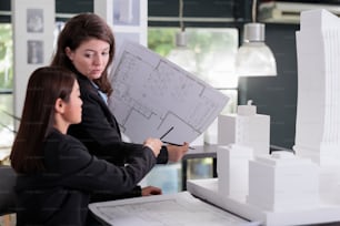 Architect and engineer holding blueprint, discussing construction project sketch, working with cad in coworking space. Employees in architecture office looking at cad together.