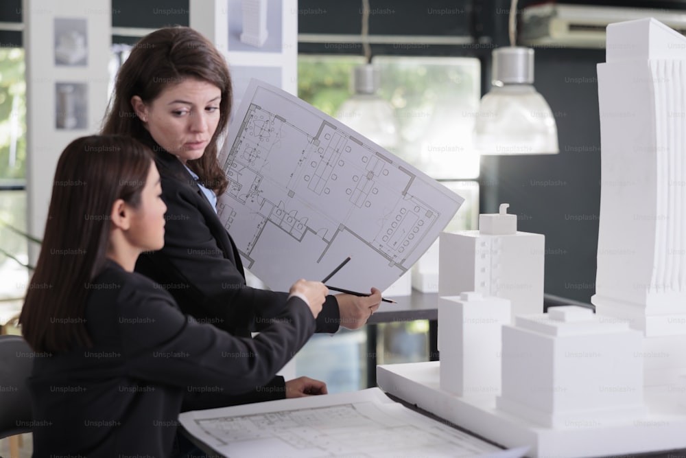 Architect and engineer holding blueprint, discussing construction project sketch, working with cad in coworking space. Employees in architecture office looking at cad together.