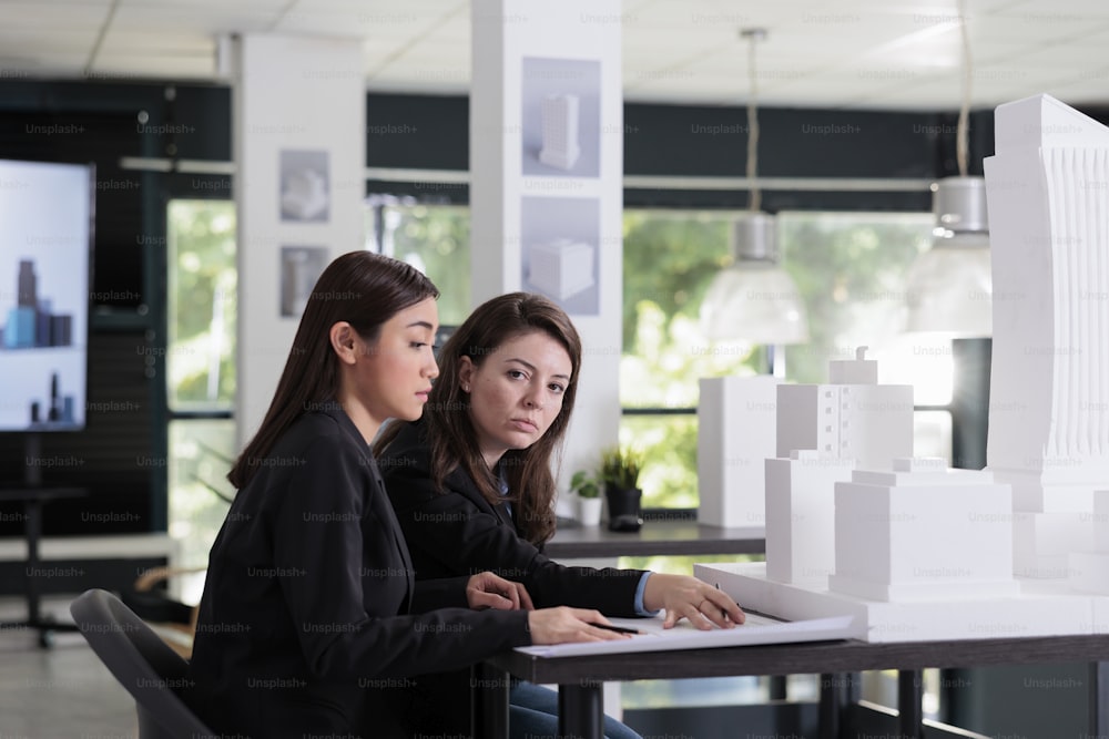 Architects working with blueprints, discussing city building 3d printed model, architectural mock up in coworking space. Employees in architecture office, real estate agency workers, engineers