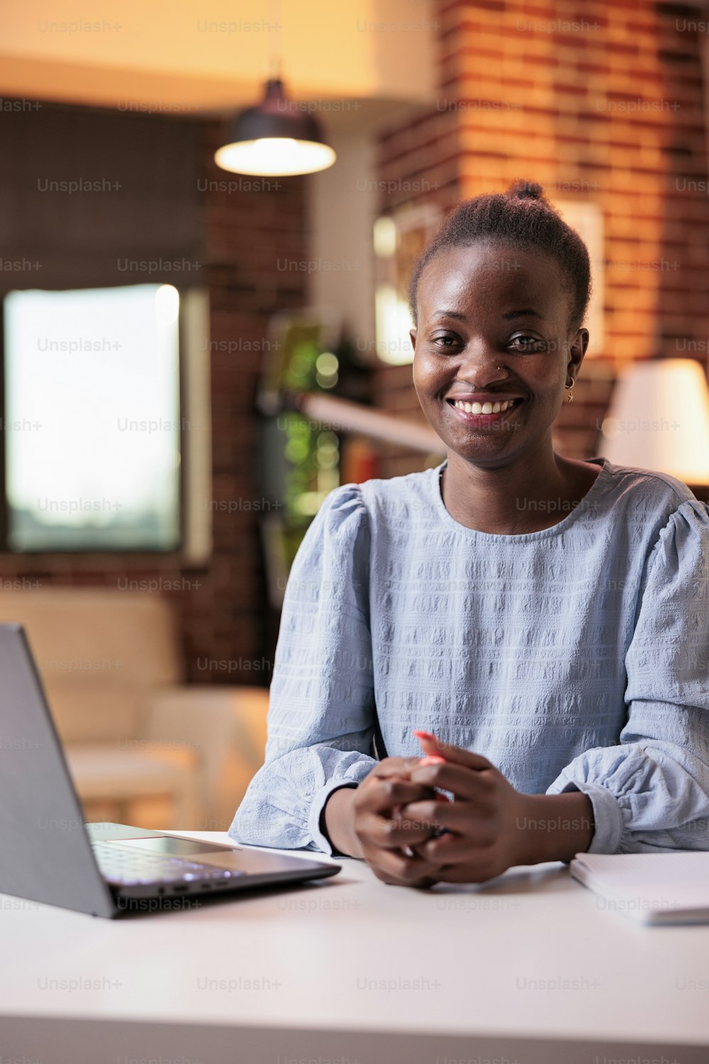 Smiling businesswoman working on laptop at workplace in home office. Young african american remote team project manager at workplace in contemporary room with big windows