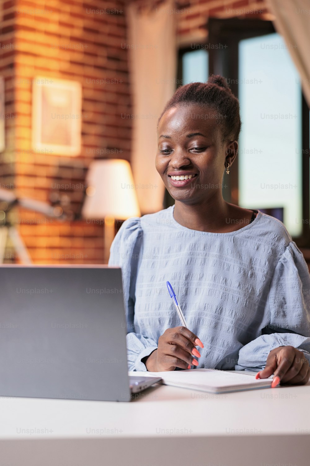 Smiling female student watching educational tutorials on laptop and taking notes in notebook. Young african american woman attending remote university online courses on internet