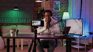 Afroamerikanischer Influencer, der einen Podcast mit einer digitalen Videokamera für einen Vlog-Beitrag in sozialen Medien aufnimmt. Content-Ersteller, der Live-Internet-Shows aus dem Heimstudio mit professionellem Equipment streamt.