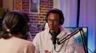 Internet podcaster reading question from laptop screen talking using microphone to influencer guest in home recording studio. African american online radio host in interview with caucasian blogger.