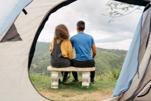 a man and a woman sitting on a bench in front of a tent