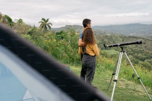 a man standing next to a telescope on top of a lush green hillside