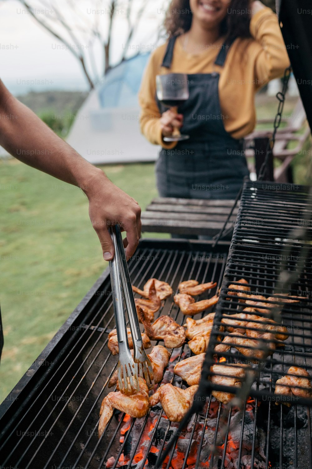 Une femme grillant du poulet sur un gril avec un verre de vin