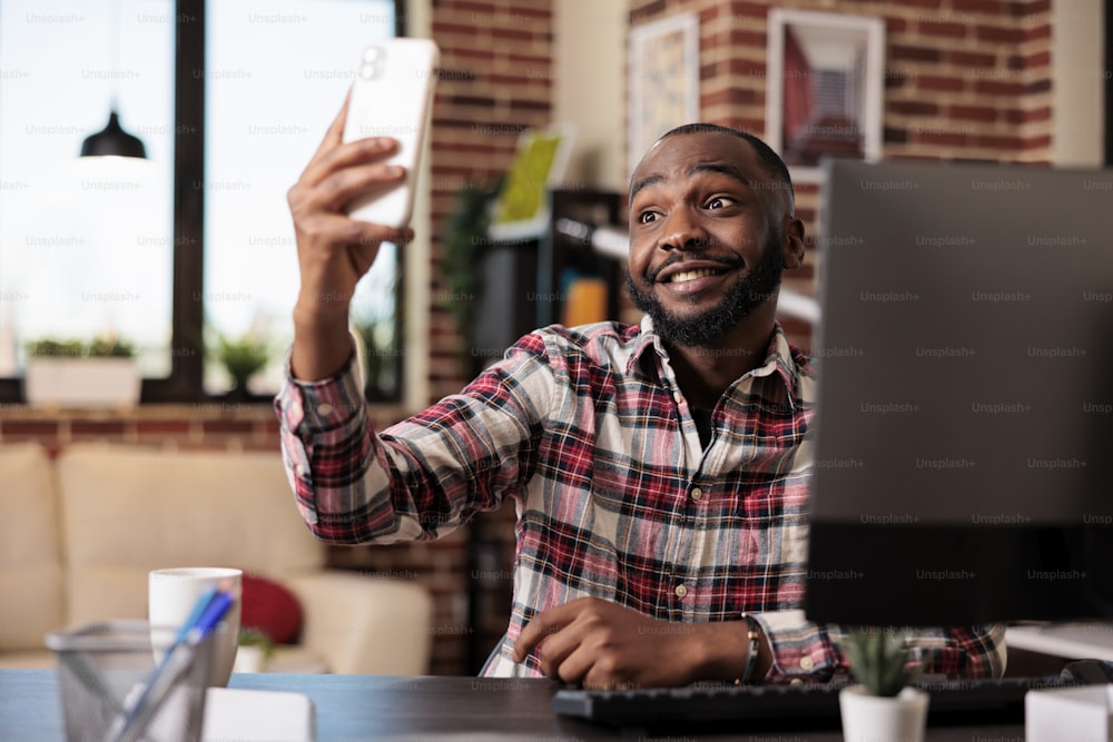 스마트폰으로 사진을 찍는 아프리카계 미국인 남성, 휴대전화를 사용하여 집 책상에서 사진을 찍는다. 프리랜서로 원격 근무를 하고 온라인 웹사이트를 사용하여 스타트업 비즈니스를 하고 있습니다.