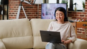 Smiling woman talking with coworker on videocall digital meeting on laptop. Joyful person working remotely while in virtual online videoconference with executive manager at home in living room.