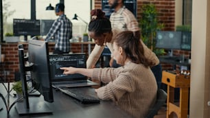 Dos codificadores de software que analizan el código fuente en busca de errores que se ejecutan en la pantalla de la computadora portátil mientras están sentados en el escritorio. Equipo de ingenieros de sistemas que trabajan en la innovación de seguridad cibernética en la concurrida sala de servidores.