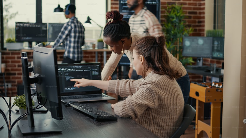 Dois codificadores de software analisando o código-fonte à procura de erros em execução na tela do laptop enquanto estão sentados na mesa. Equipe de engenheiros de sistema trabalhando na inovação de segurança cibernética em sala de servidores ocupada.