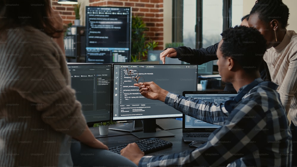 Los desarrolladores de software que discuten sobre la compilación de código fuente descubren errores y piden explicaciones al resto del equipo frente a múltiples pantallas que ejecutan algoritmos. Programadores haciendo trabajo en equipo.