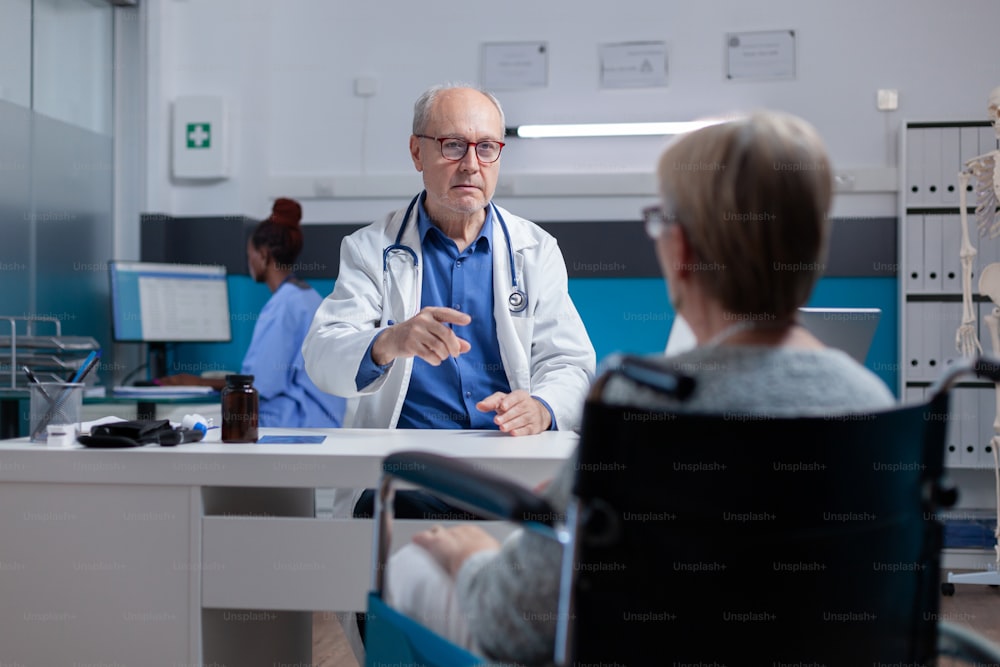 Doctor attending medical consultation with woman sitting in wheelchair at clinic. Physician having conversation about diagnosis after examination with patient with physical disability.