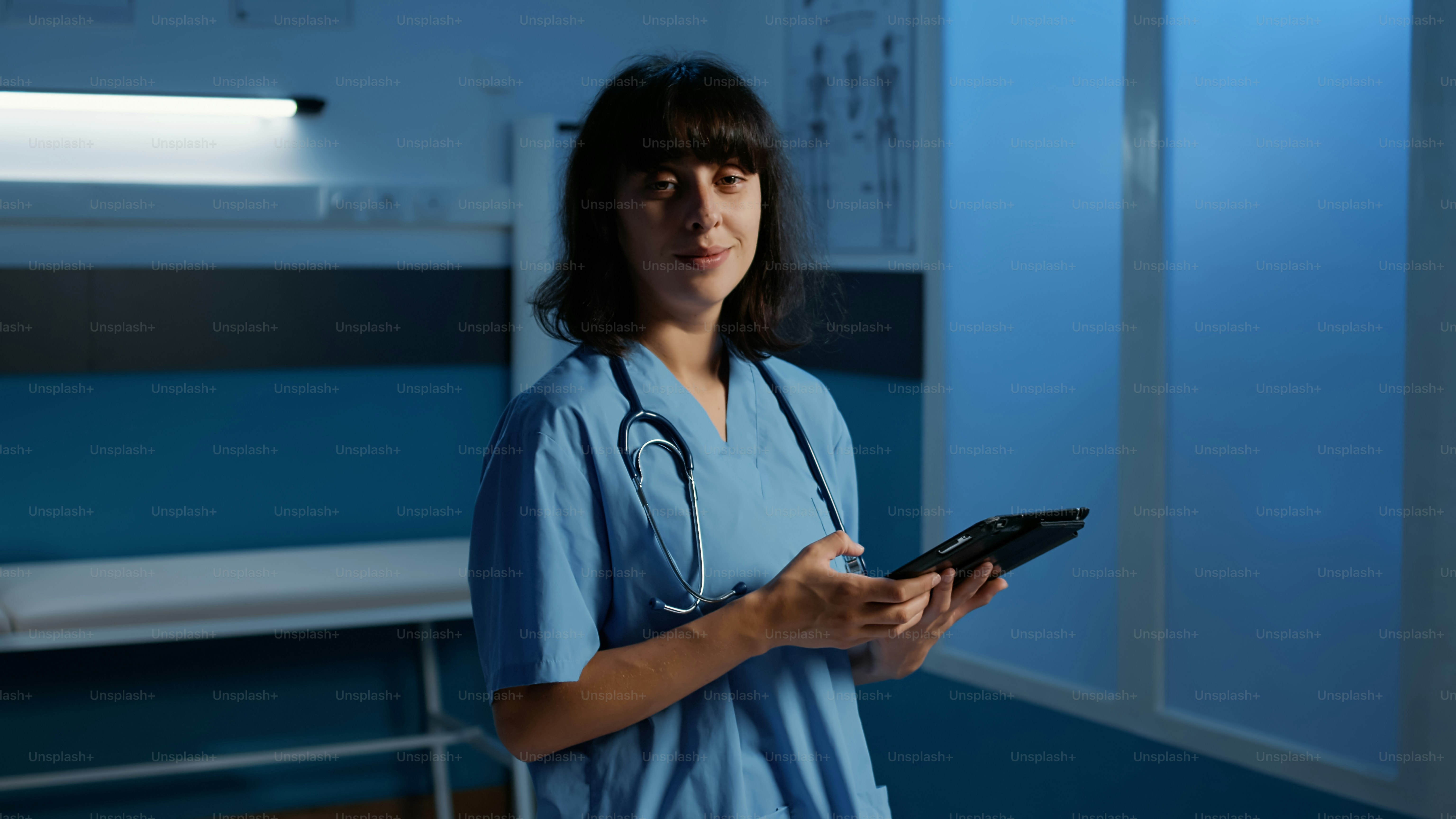 Arzthelferin in medizinischer Uniform, die während der Untersuchung eine Gesundheitsbehandlung auf einem Tablet-Computer eintippt, besucht einen Termin im Krankenhausbüro spät in der Nacht. Müde Krankenschwester, die nach Feierabend in der Klinik arbeitet