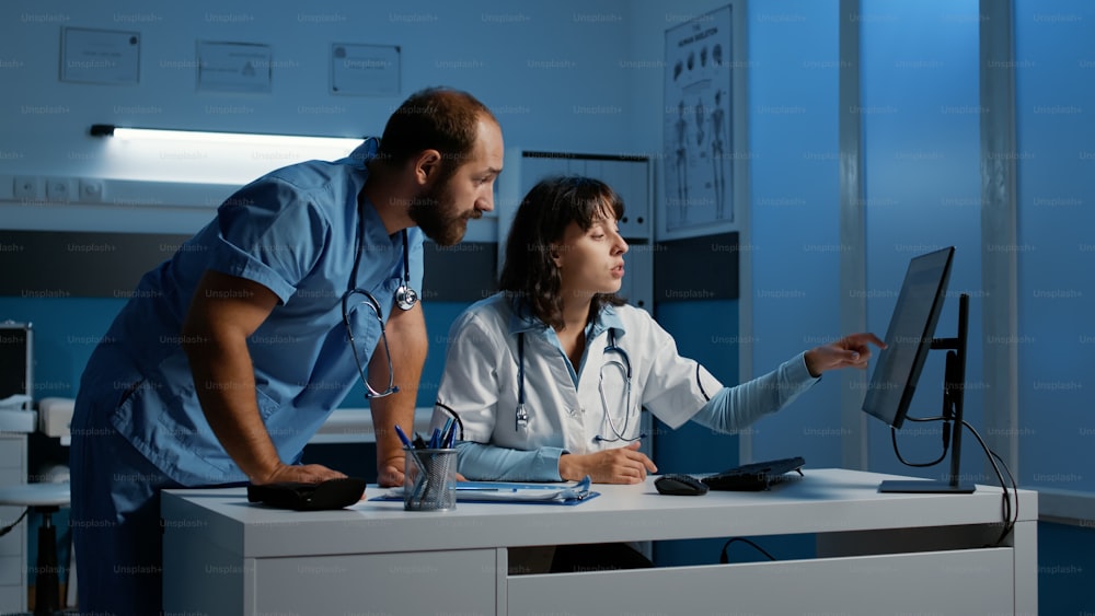 Clinical staff looking at computer monitor analyzing patient medical expertise while discussing medication treatment to help cure disease. Physician and nurse working night shift in hospital office