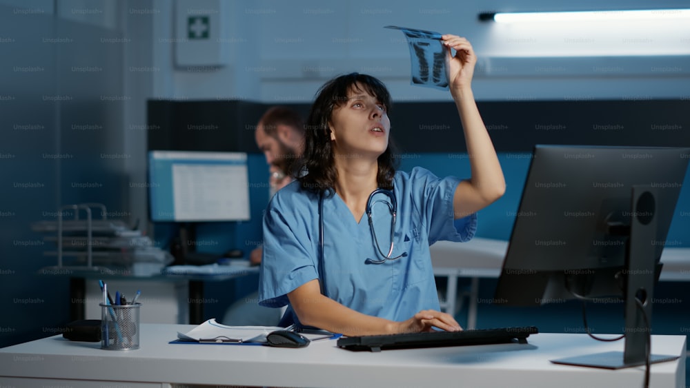 Médico enfermeiro analisando radiografia de pacientes digitando perícia médica em computador trabalhando ao longo de horas no consultório do hospital. Assistente de verificação do relatório do paciente planejando o tratamento medicamentoso. Serviço de medicina