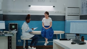 Young patient on bed talking to doctor for annual checkup visit and examination. Medic with healthcare information consulting woman at medical appointment. Specialist doing consultation