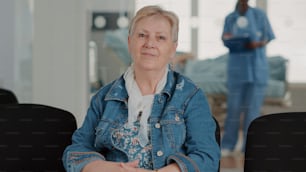 Portrait of senior patient preparing for medical appointment in waiting area. Close up of retired woman sitting in facility reception room to do checkup appointment with physician.