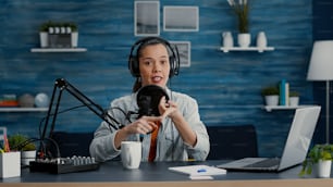 Digital content creator in studio at home recording daily vlog while telling stories. Creative social media influencer presenting to audience world events while sitting in studio living room.