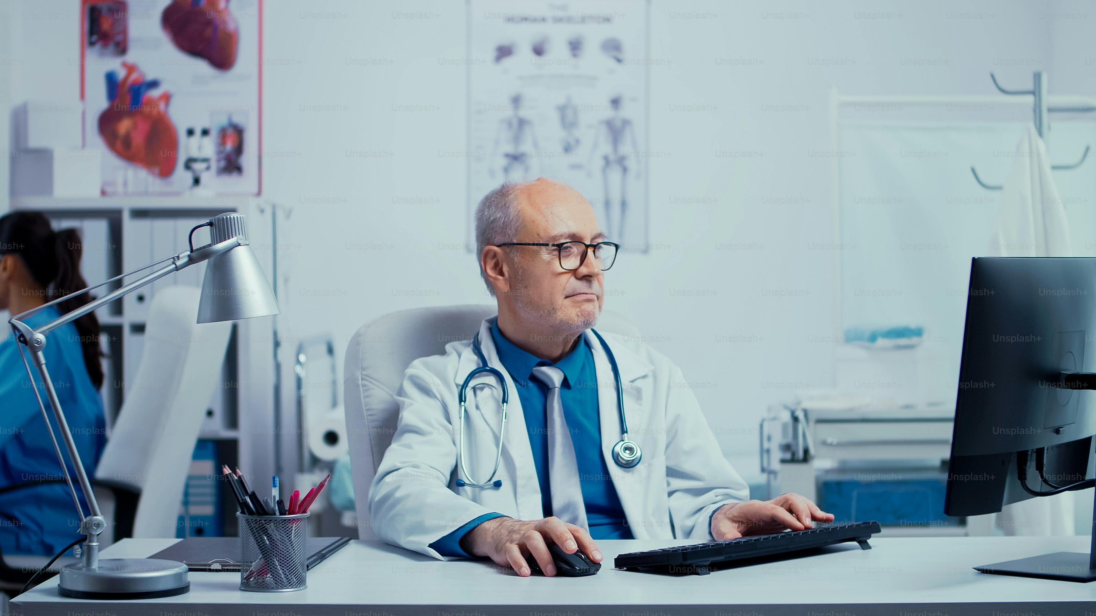 Working in modern private clinic with nurse checking X Rays in the back while the doctor is typing at PC in front. Modern clinic healthcare system physician specialist practitioner in uniform specialist working