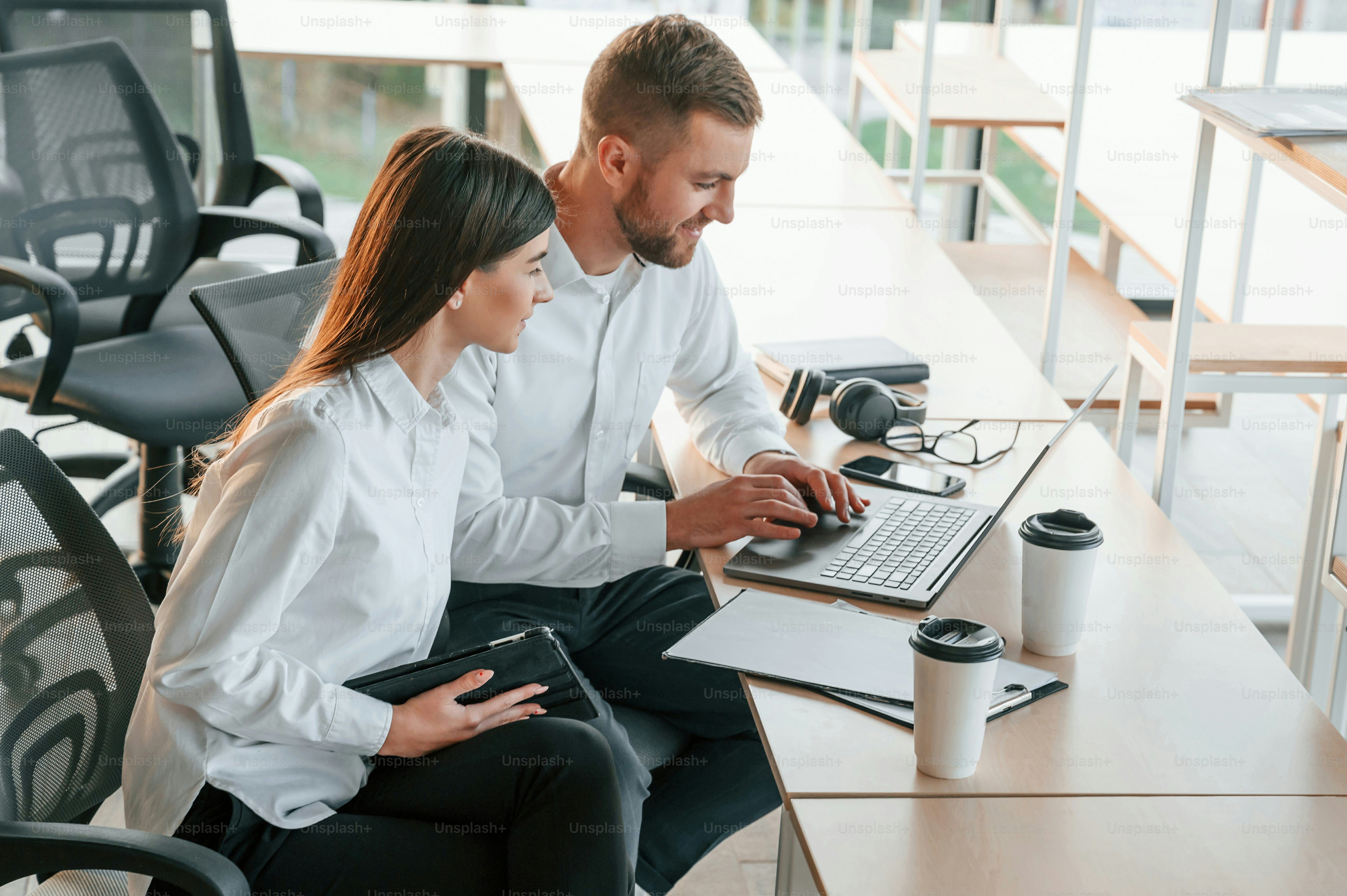 Seduto al tavolo con il computer portatile. L'uomo e la donna lavorano insieme nell'ufficio moderno.