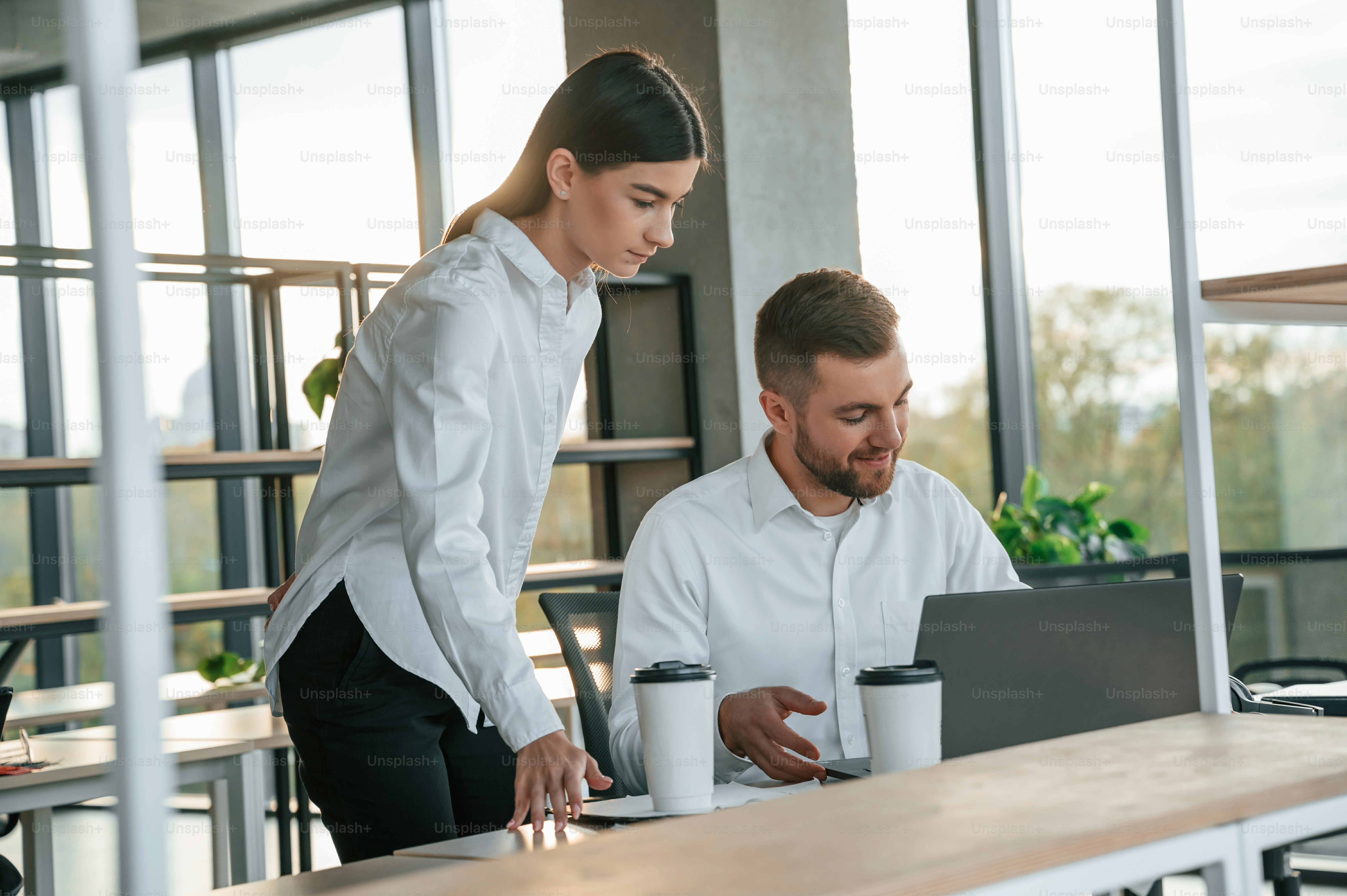 Utilizzando il computer portatile. L'uomo e la donna lavorano insieme nell'ufficio moderno.