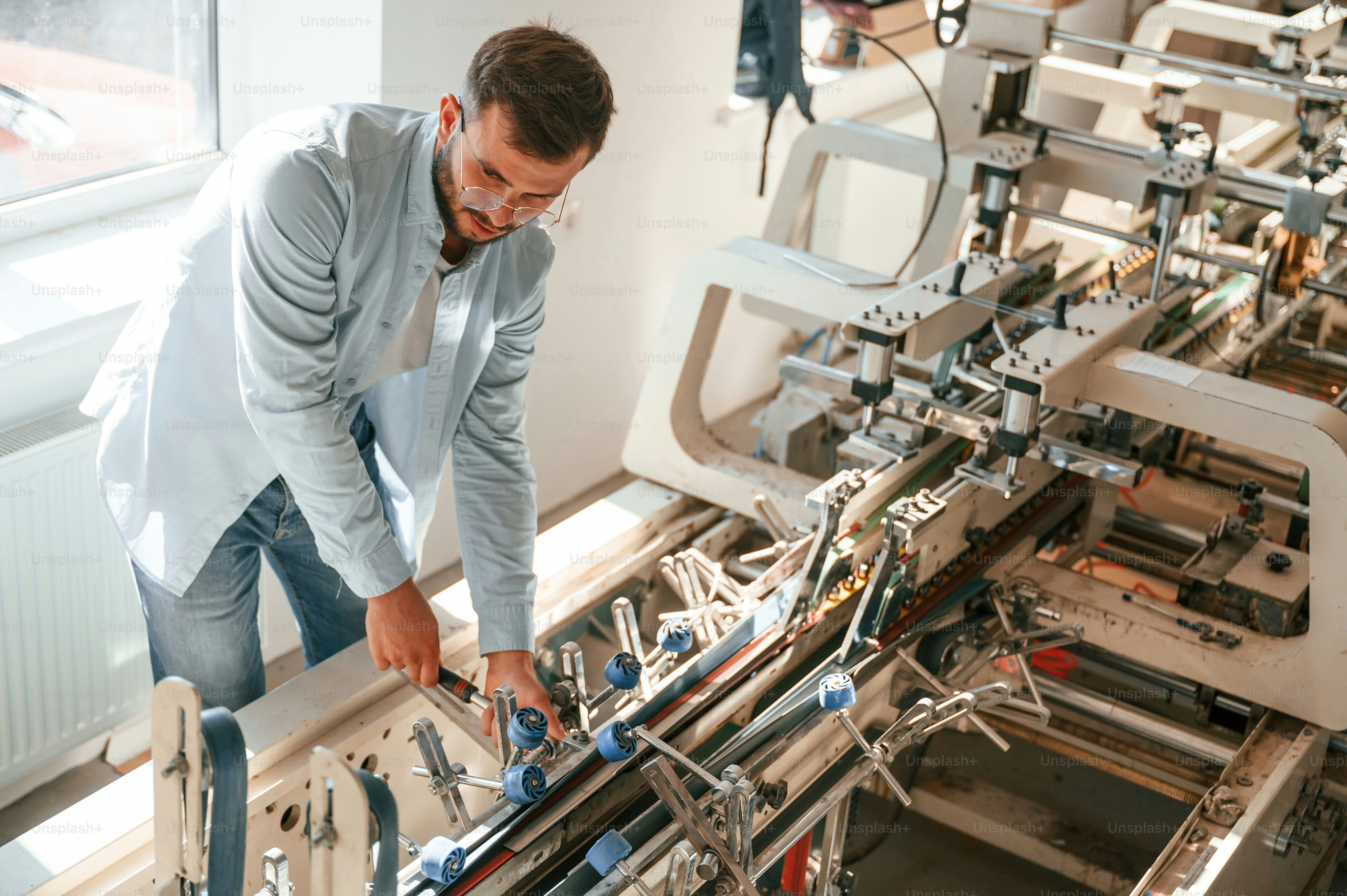 Setting up a printing machine. Typography worker in white clothes is indoors.