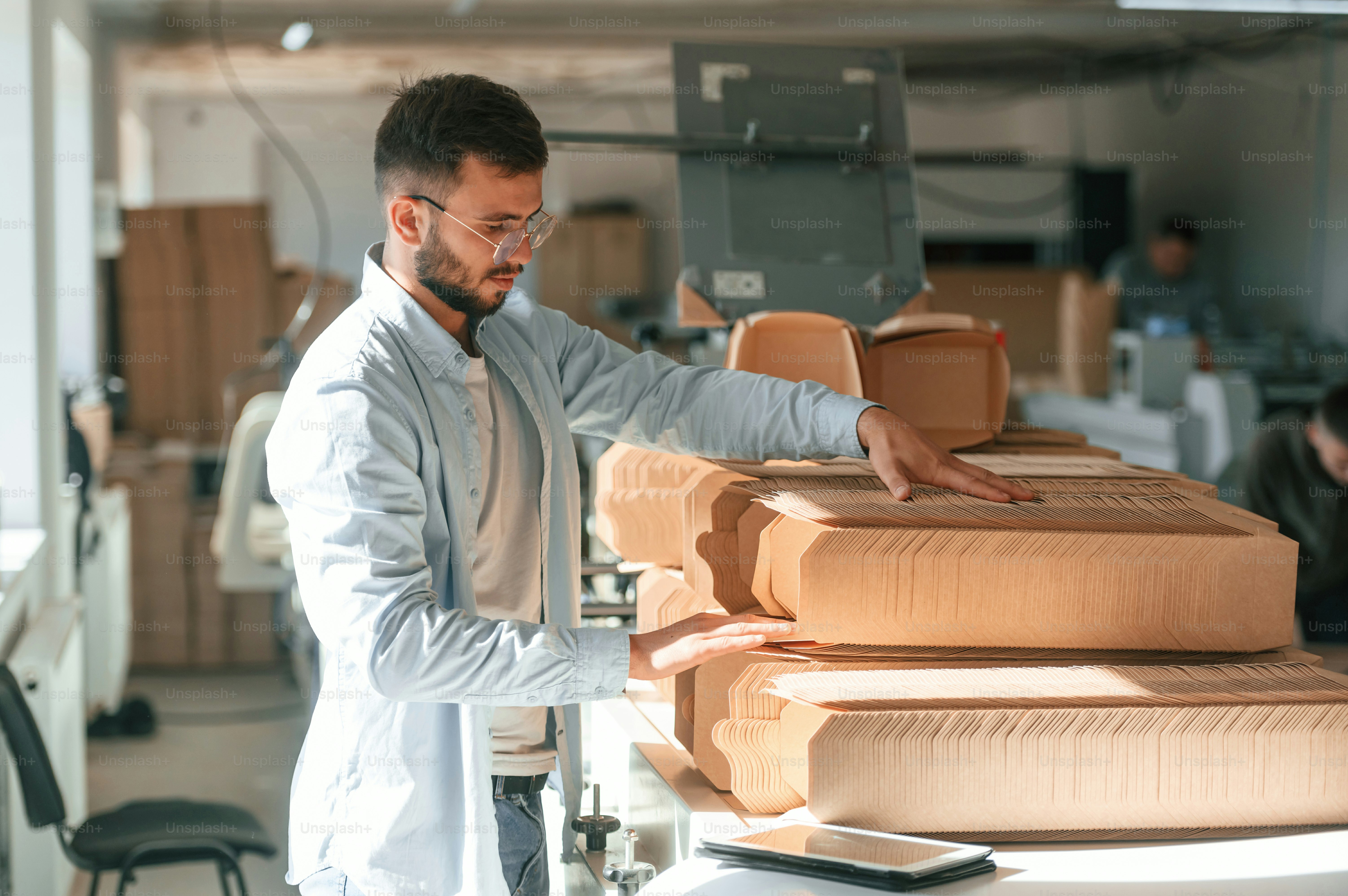 Print house worker in white clothes is indoors taking bunch of wooden sheets.
