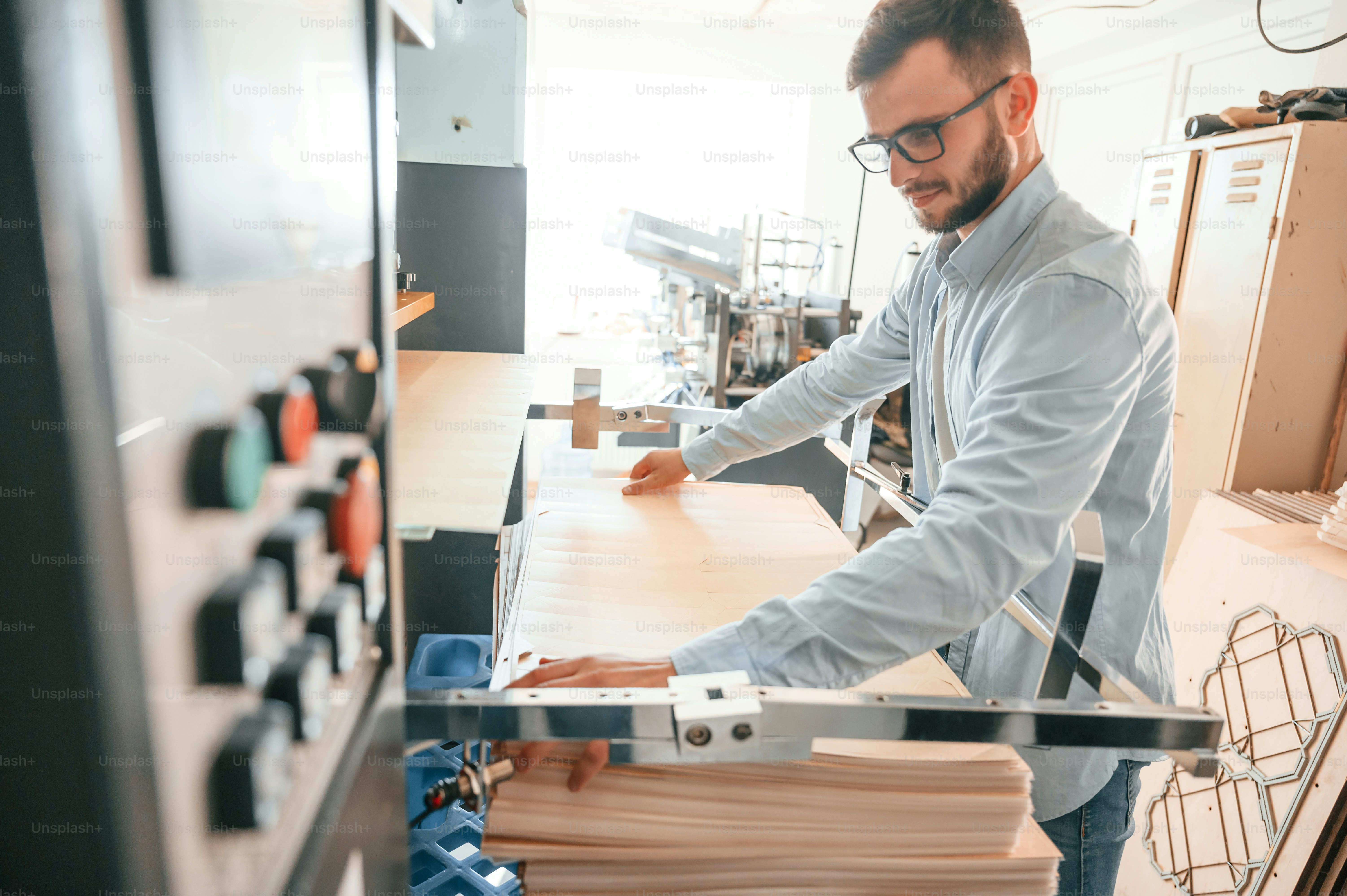 Working with wooden sheets. Man in print house that in white clothes is indoors.